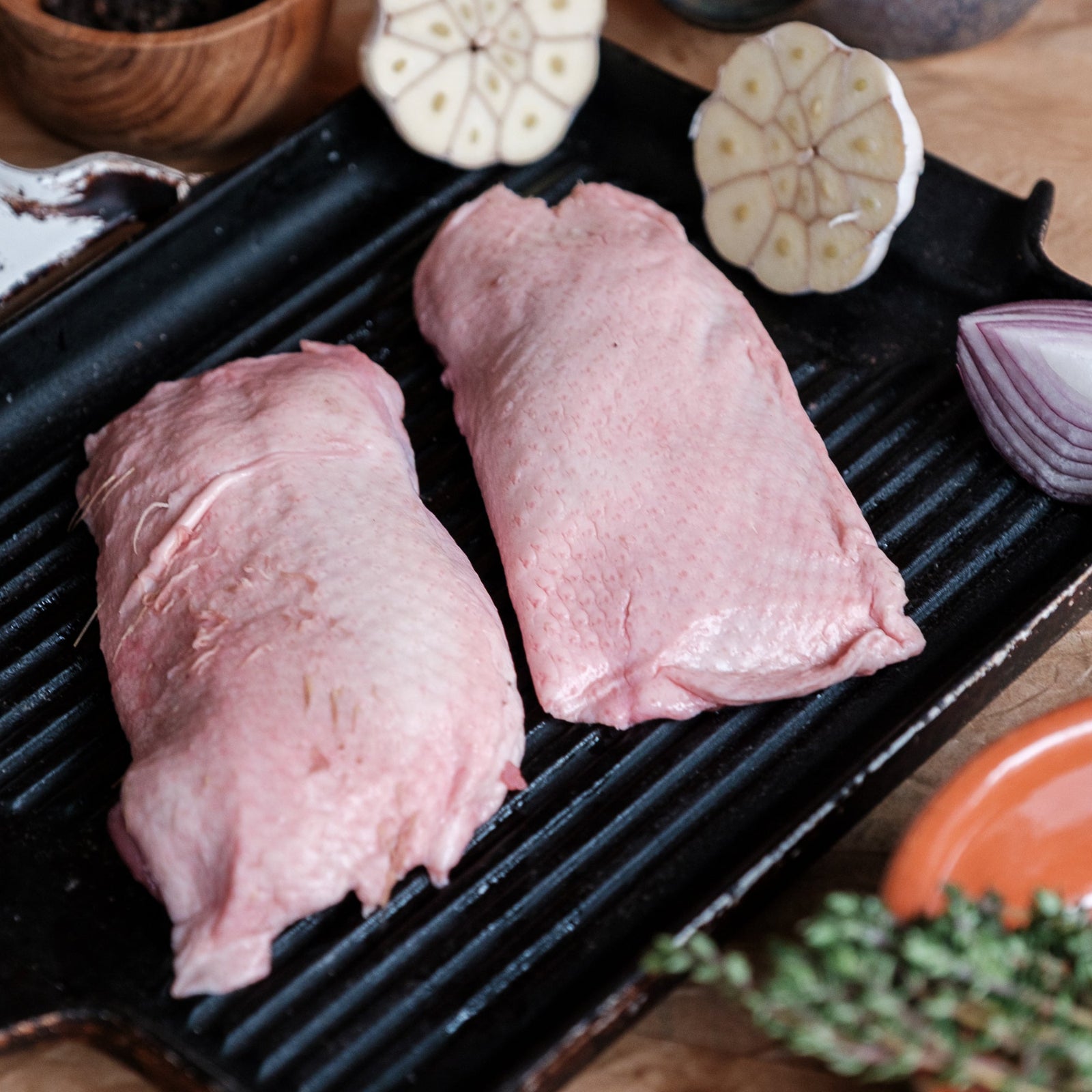 Two duck breast on a grill pan with vegetables on a wooden surface