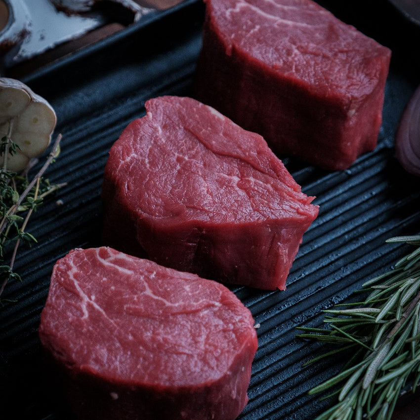 Raw fillet steaks on a grill with rosemary and a wooden background