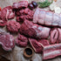Assorted cuts of raw meat on a wooden surface with vegetables.