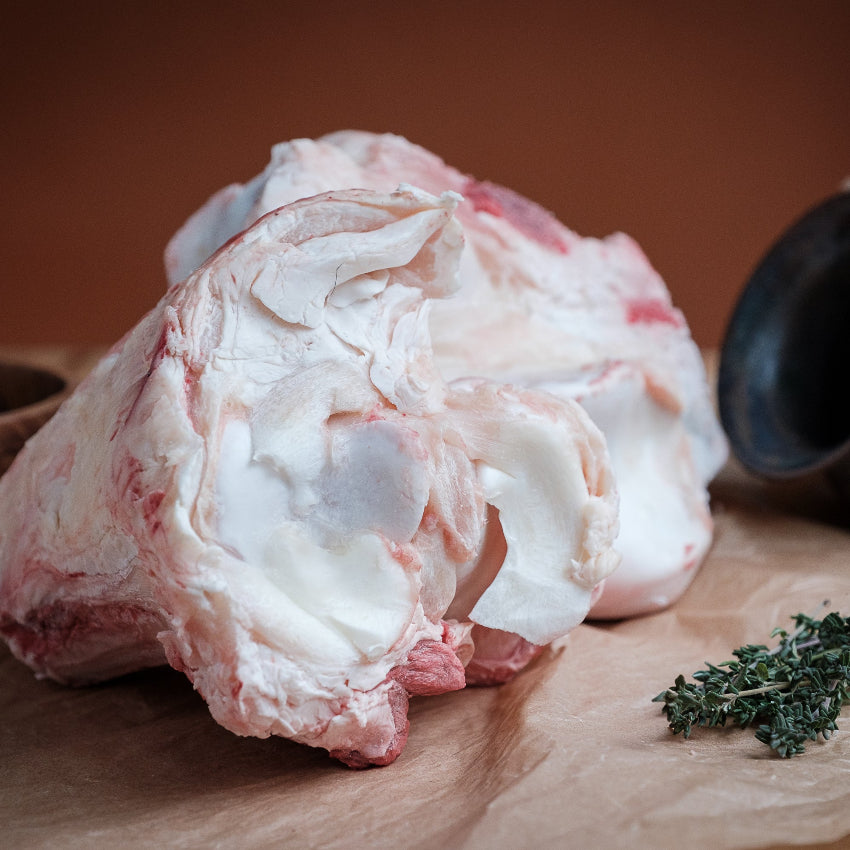 Raw beef knuckle bone on a wooden surface with herbs and a pot in the background
