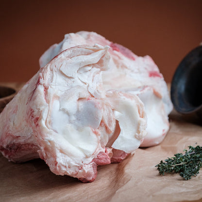Raw beef knuckle bone on a wooden surface with herbs and a pot in the background