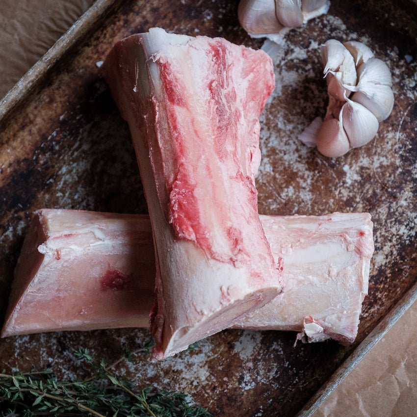 Raw beef marrow bones on a baking tray with garlic and herbs