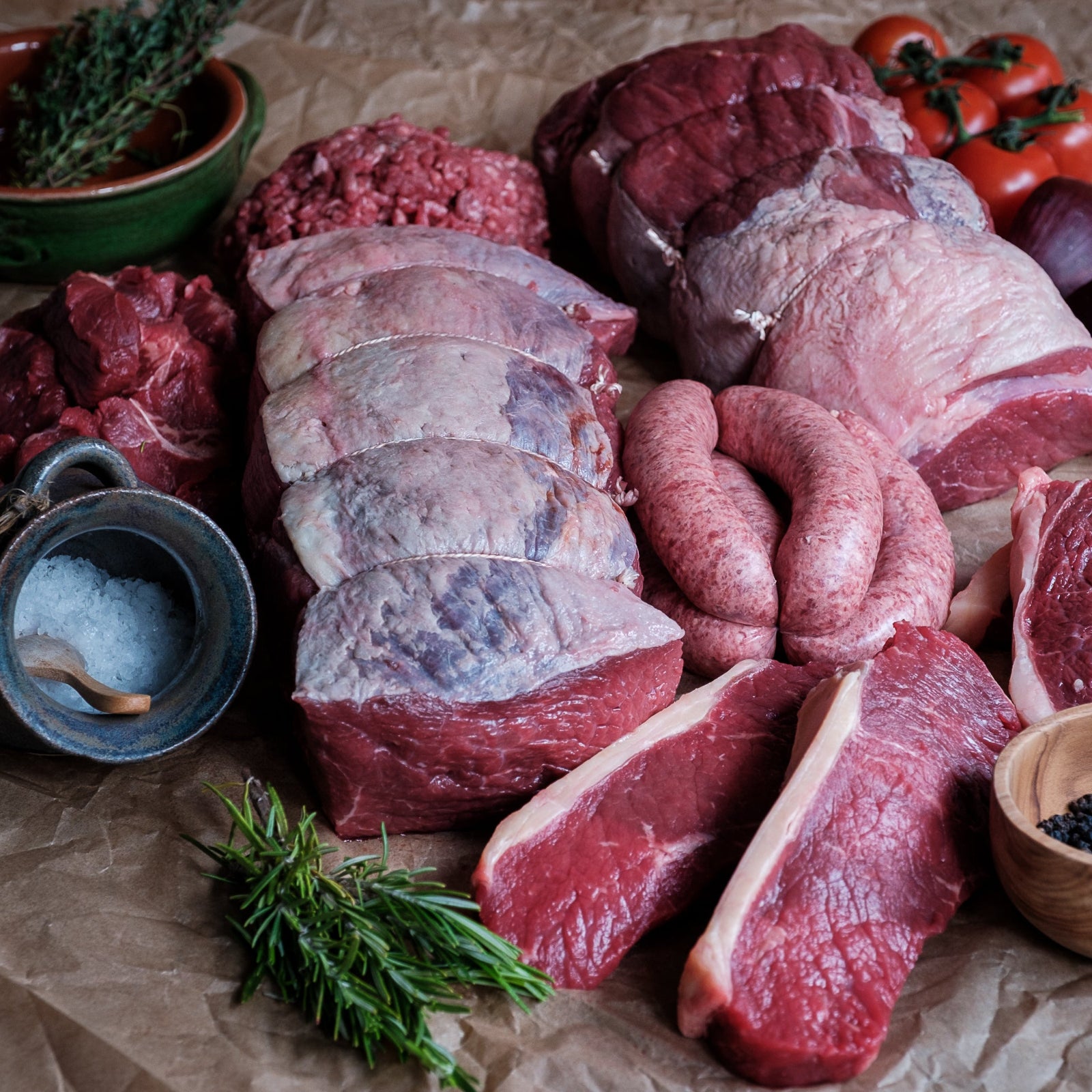 Assorted raw meats on a rustic surface with herbs and spices.