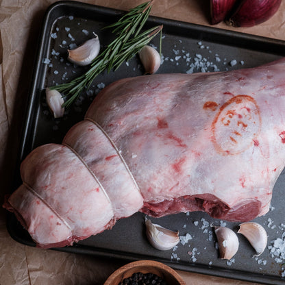Raw carvery lamb leg on a baking tray with garlic and rosemary, on a rustic background