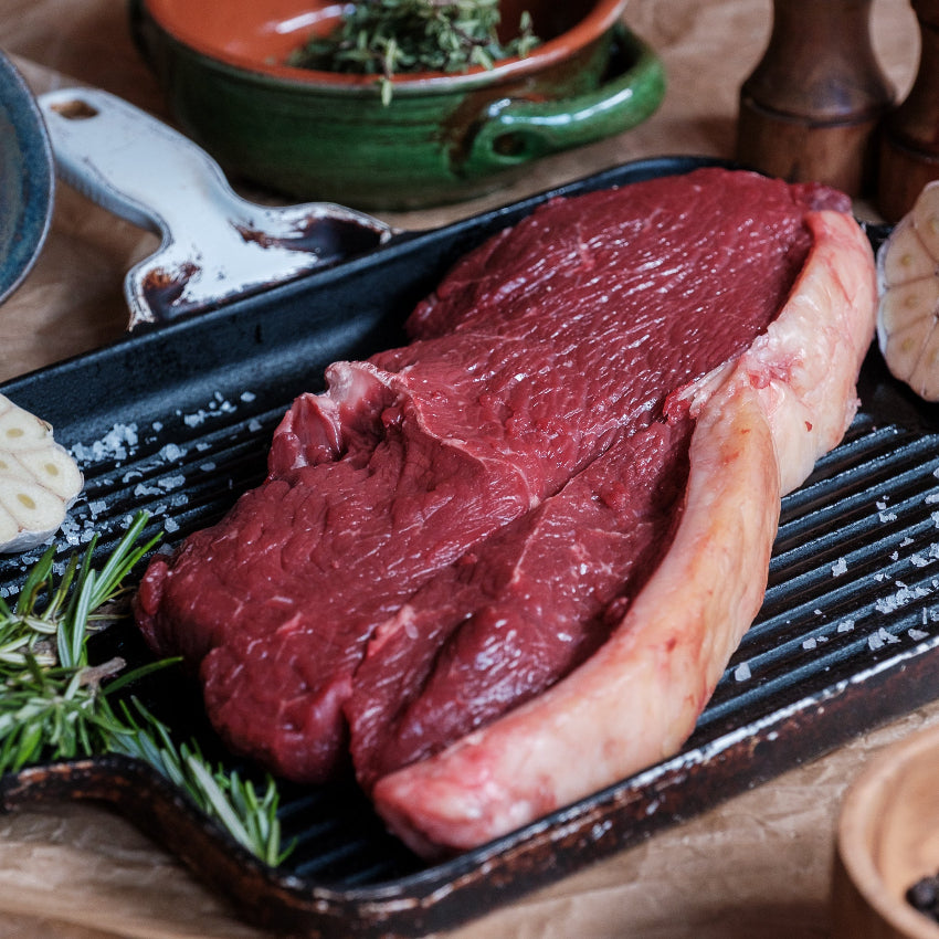 Raw carvery rump steak on a grill pan with herbs and spices on a rustic background