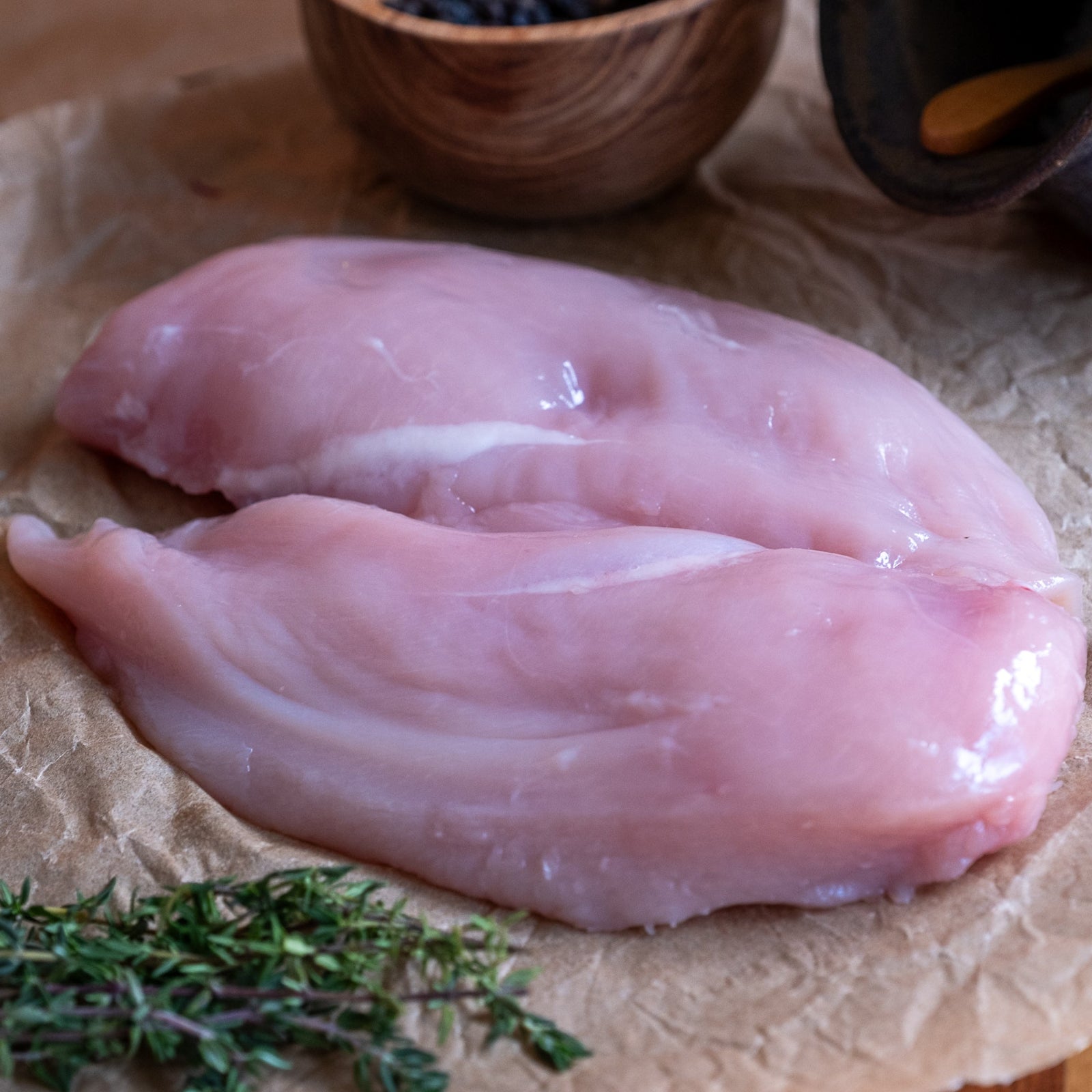 Raw chicken fillet on brown paper with a red onion and thyme sprigs.