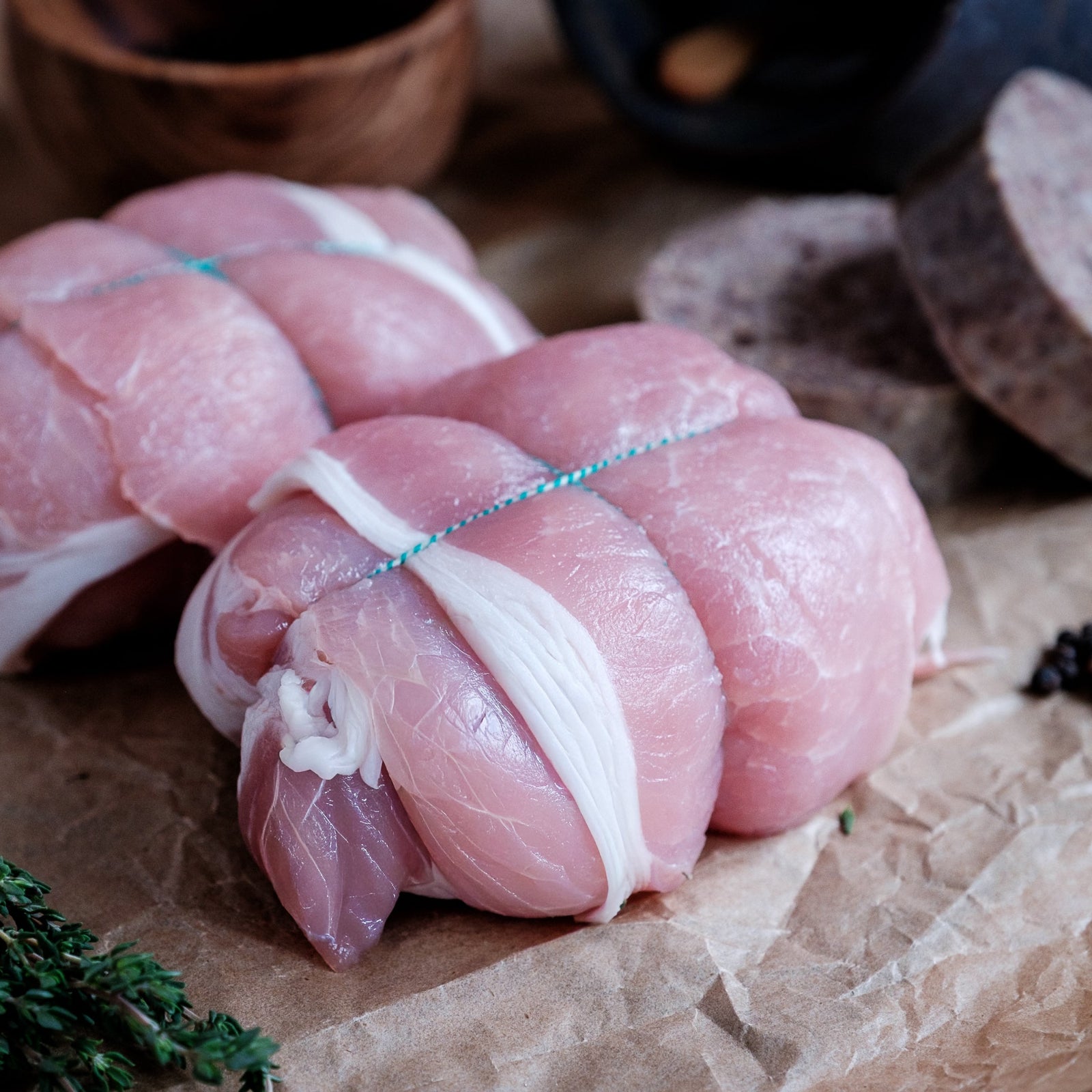 Raw chicken olive tied with string on a wooden surface with herbs and a bowl in the background