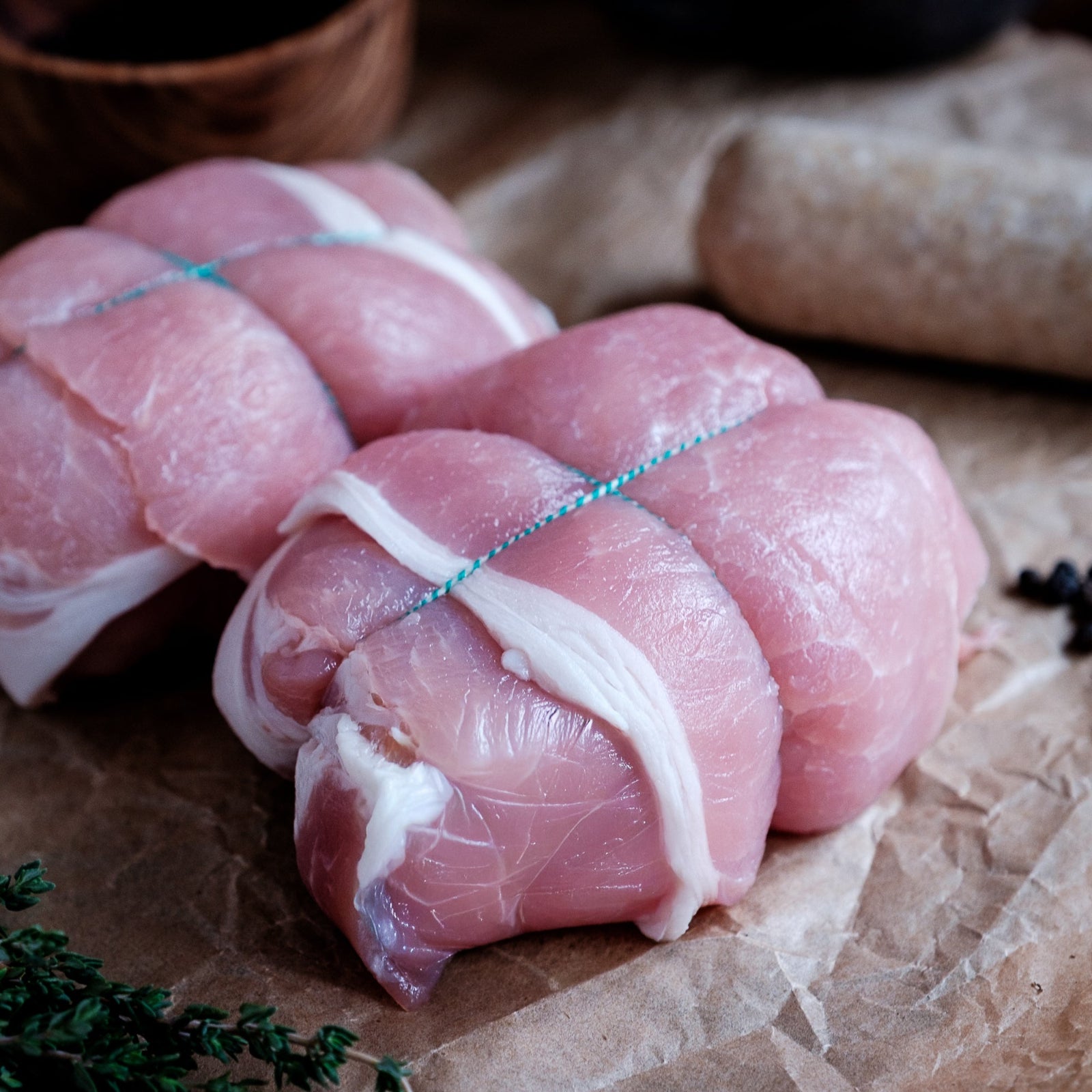 Raw chicken olives tied with string on a rustic surface with herbs and spices.
