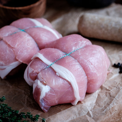 Raw chicken olives tied with string on a rustic surface with herbs and spices.