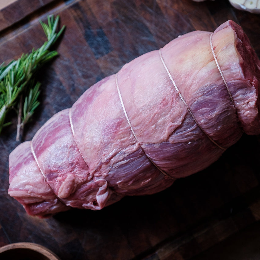Raw rolled chuck roast on a wooden cutting board with herbs