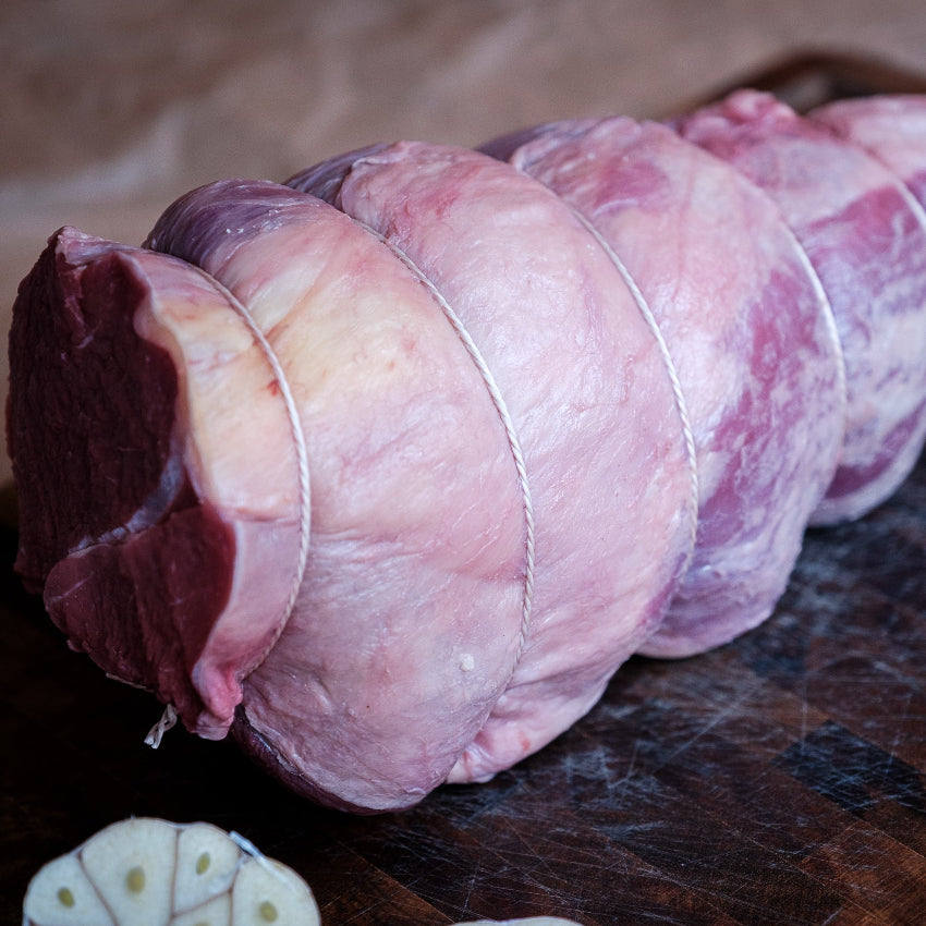 Raw chuck roast roll on a wooden board with herbs
