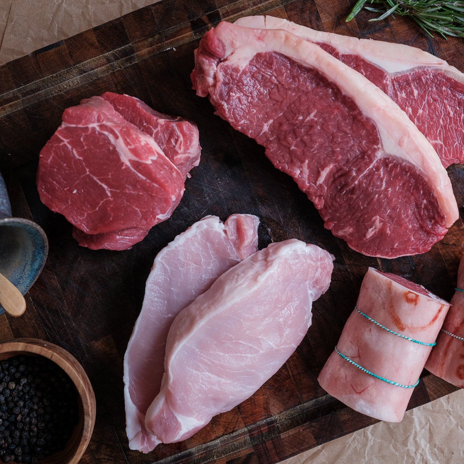 Assorted raw meats on a wooden cutting board with herbs and spices.