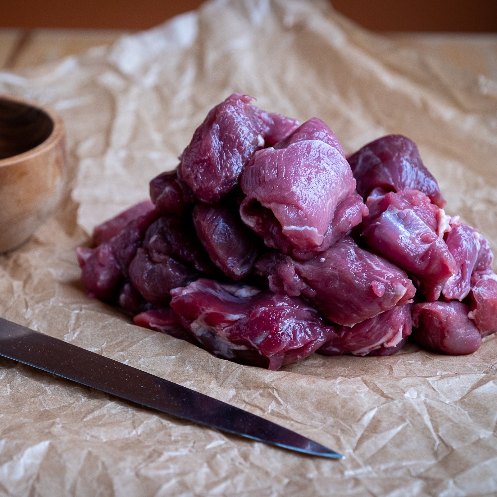 Diced Lamb on crumpled paper with a wooden bowl and knife.