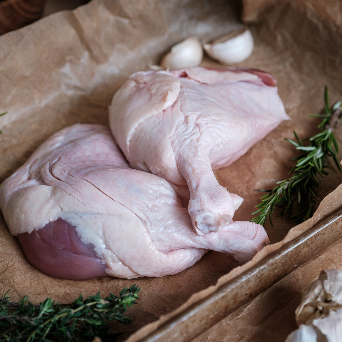 Raw duck legs with herbs and garlic on brown paper
