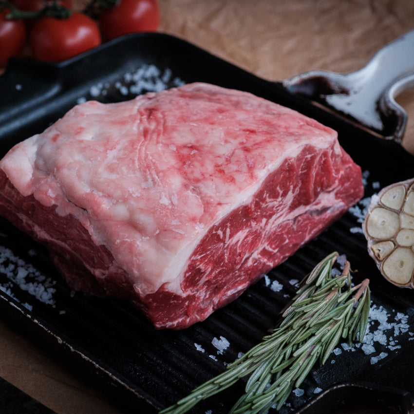 Raw feather blade on a grill pan with garlic and rosemary, on a wooden surface.