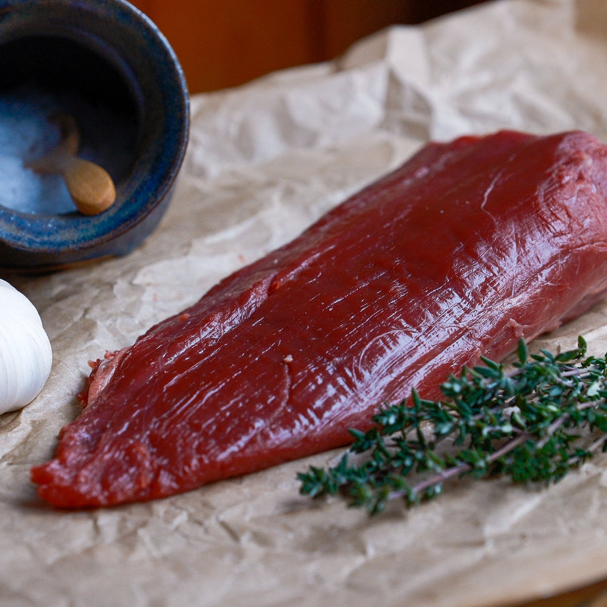 Raw beef fillet tail with garlic and thyme on a wooden surface