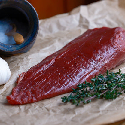 Raw beef fillet tail with garlic and thyme on a wooden surface