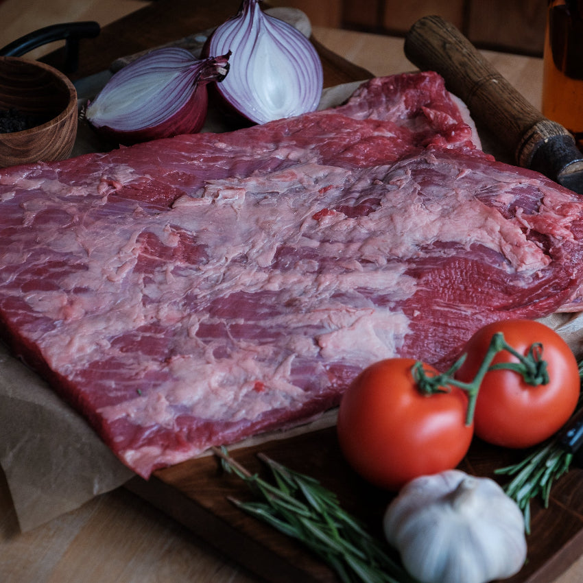 Flat Beef Brisket on a cutting board with vegetables and a bottle of oil.