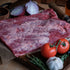Flat Beef Brisket on a cutting board with vegetables and a bottle of oil.