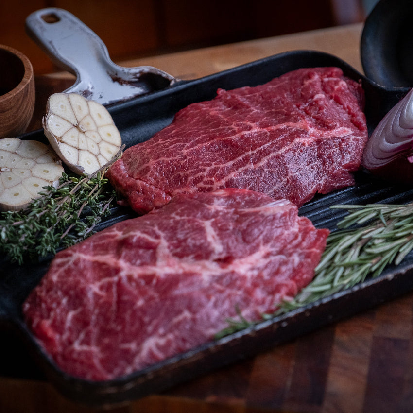 Flat Iron steaks on a grill pan with herbs and garlic on a wooden surface