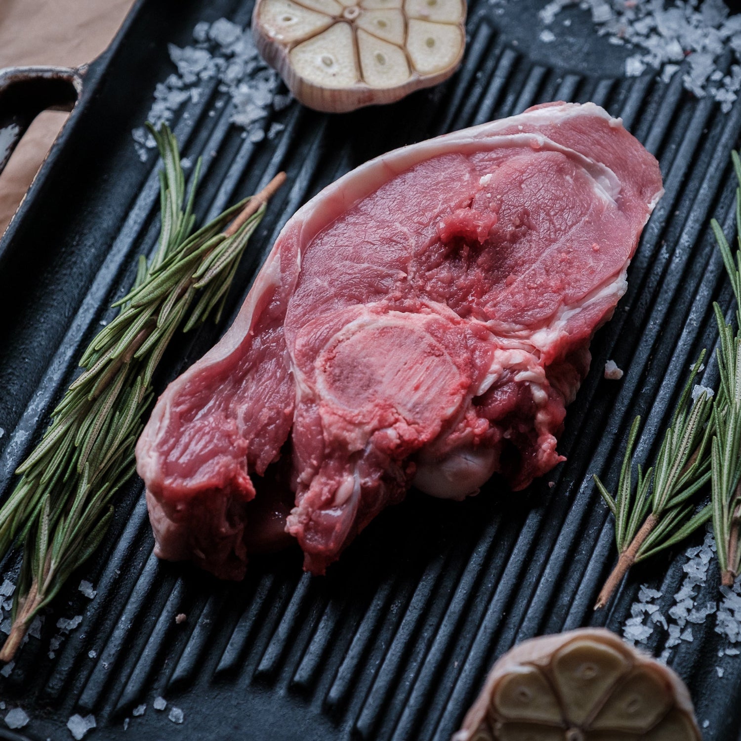 Raw lamb gigot chop on a grill pan with herbs and salt