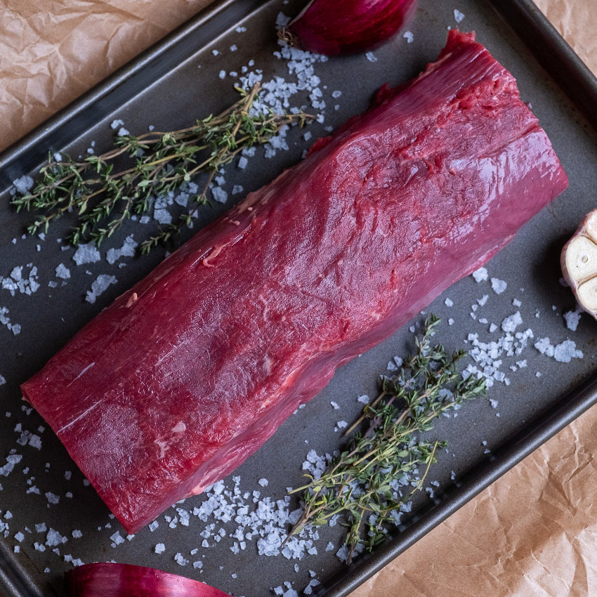 Larder Trim beef fillet on a tray with herbs and garlic on a brown paper background