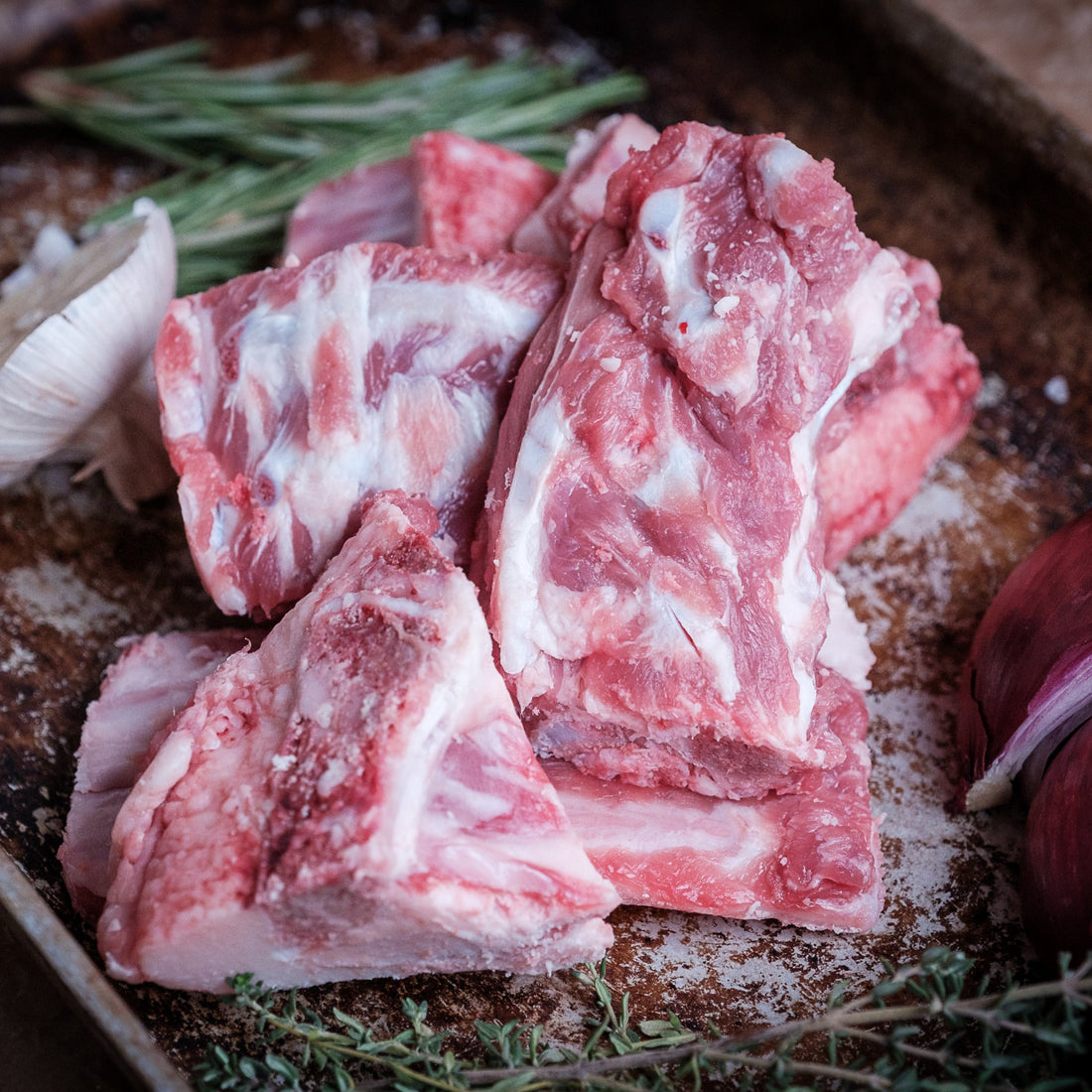 Raw lamb bones on a baking tray with garlic, onions, and herbs