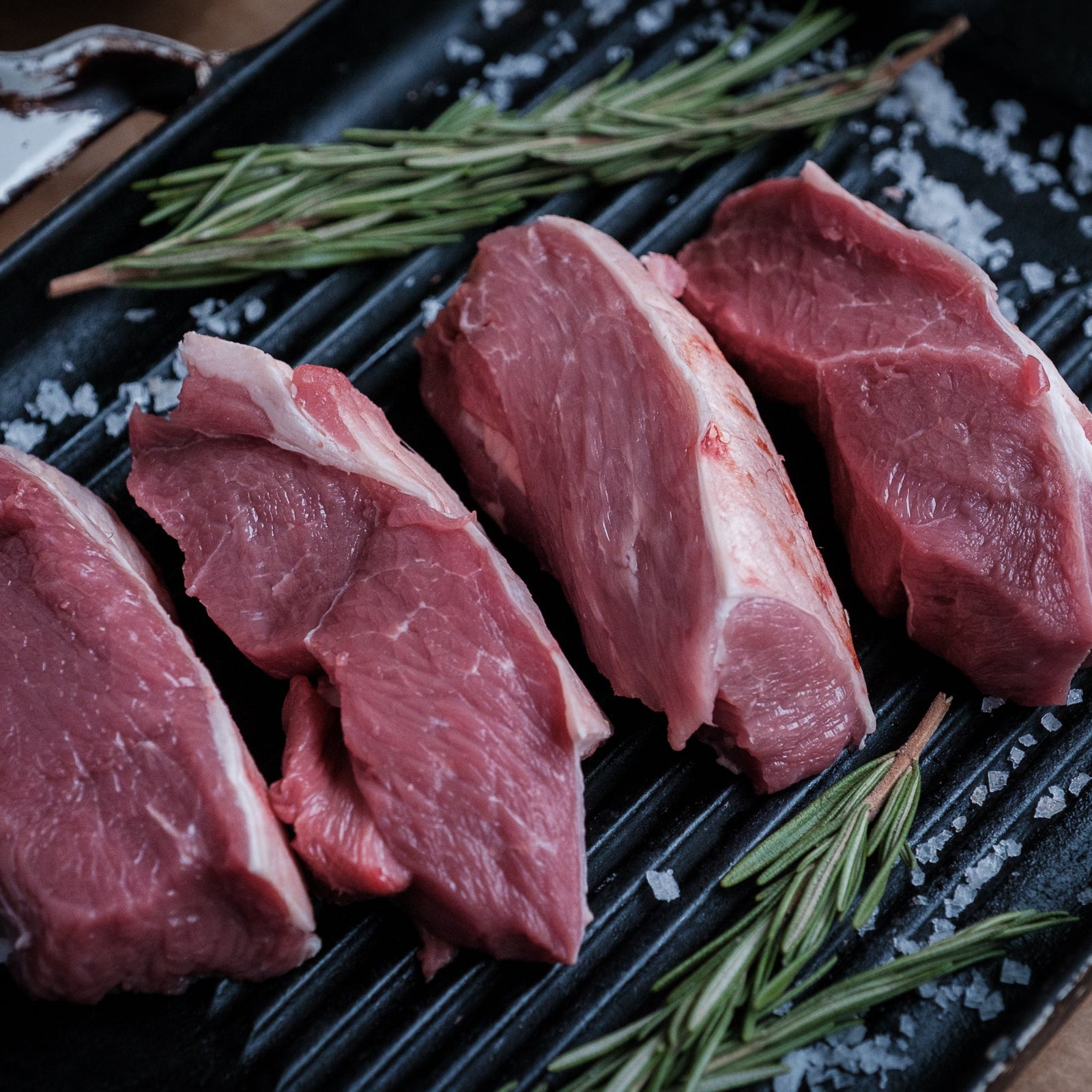 Raw lamb leg steaks on a grill with rosemary and salt