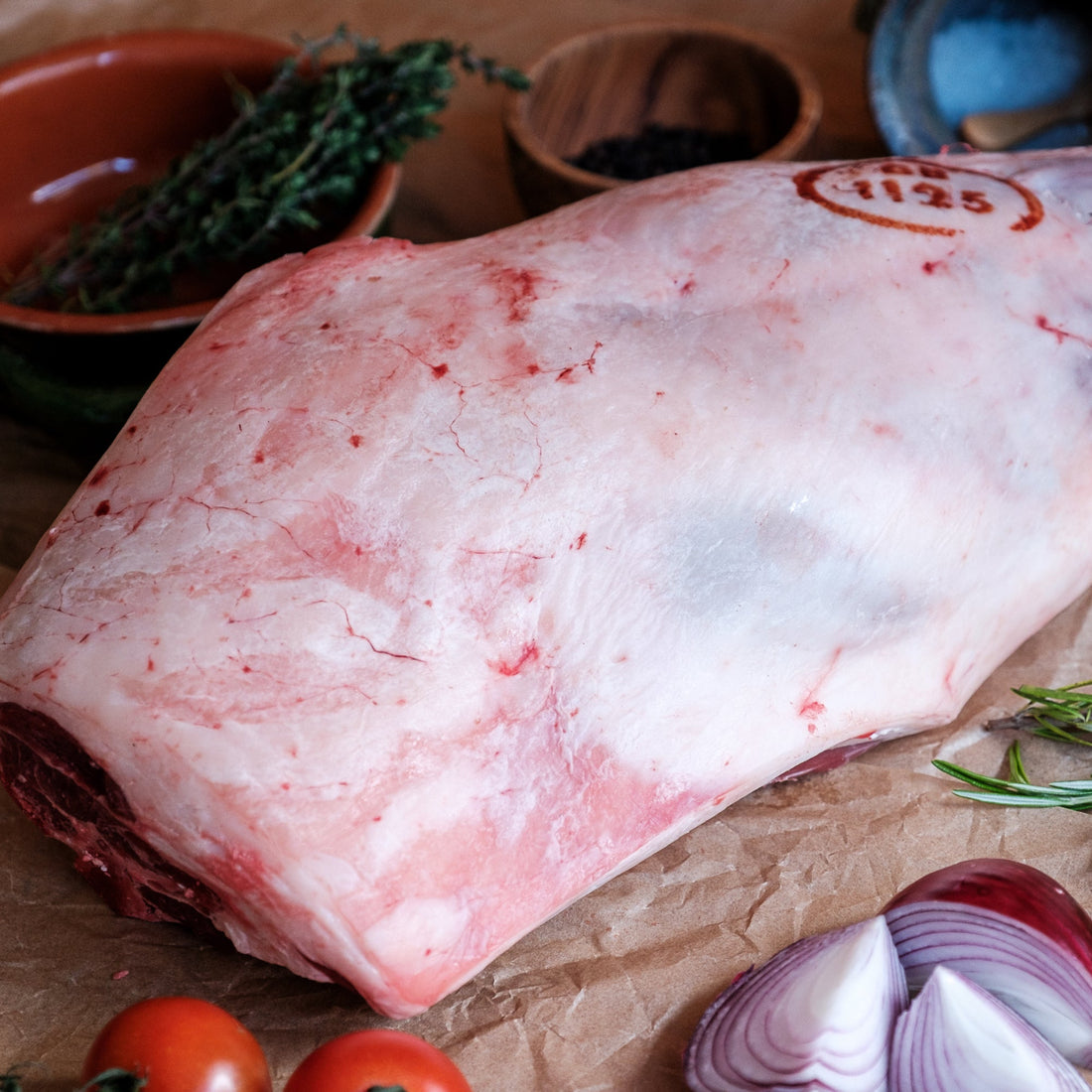 Raw leg of lamb with herbs and vegetables on a rustic background