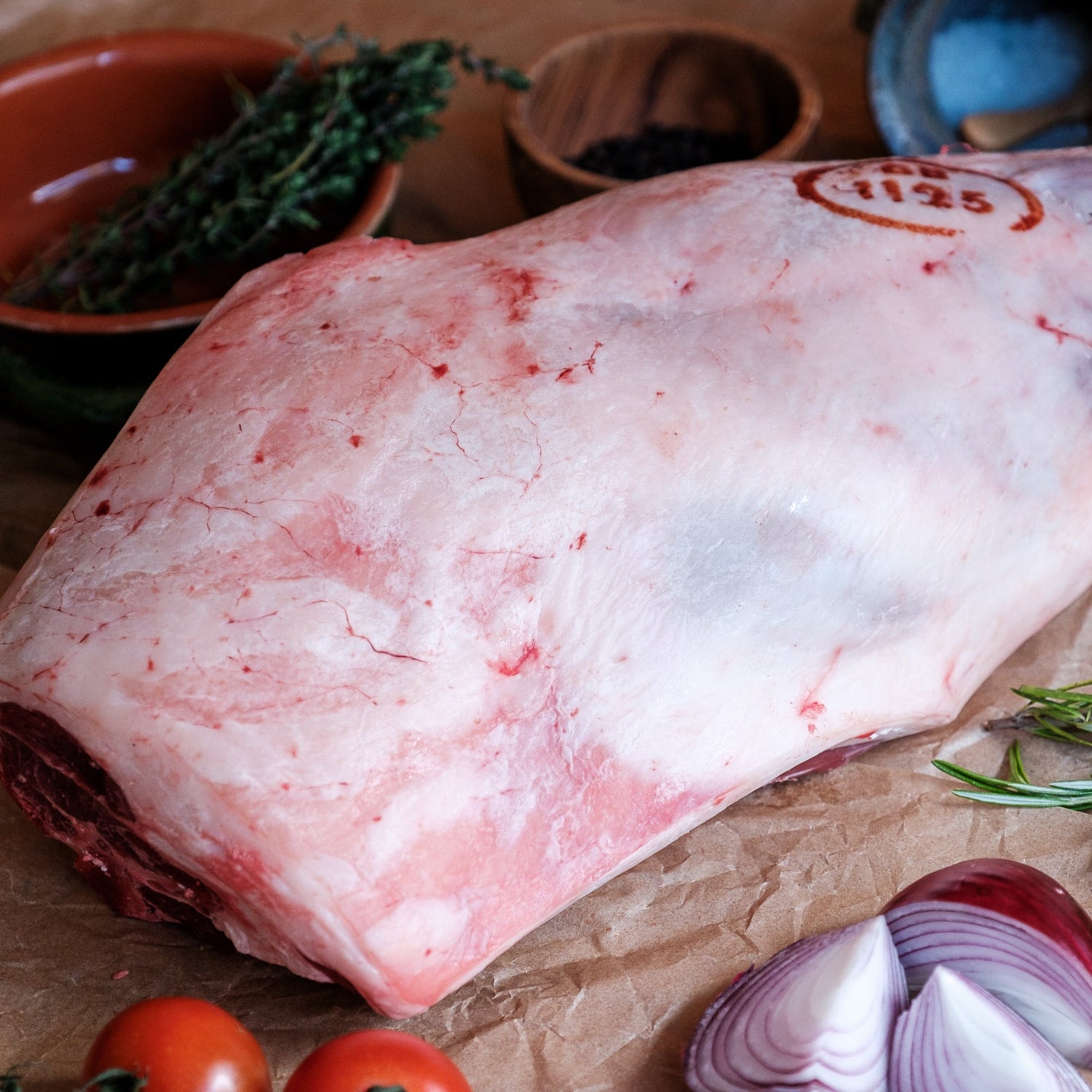Raw leg of lamb with herbs and vegetables on a rustic background