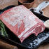 Raw lamb loin on a black grill pan with herbs and garlic on a wooden surface