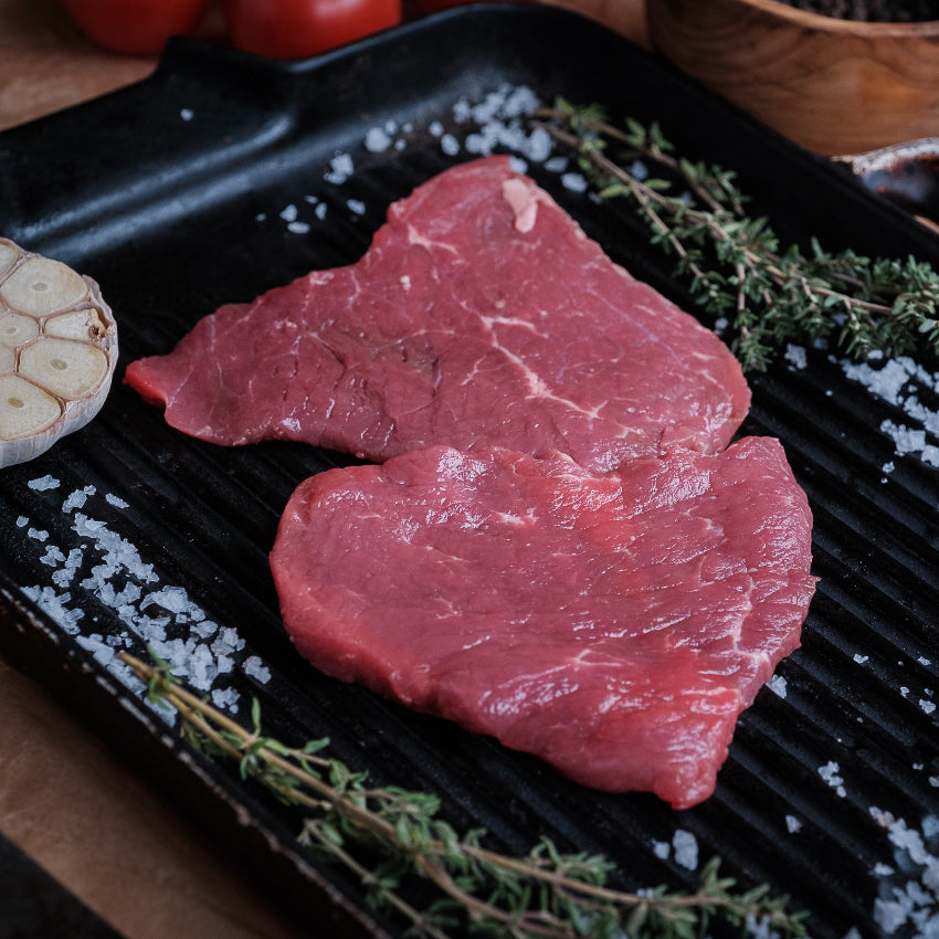 Minute steak on a grill pan with herbs and garlic cloves.