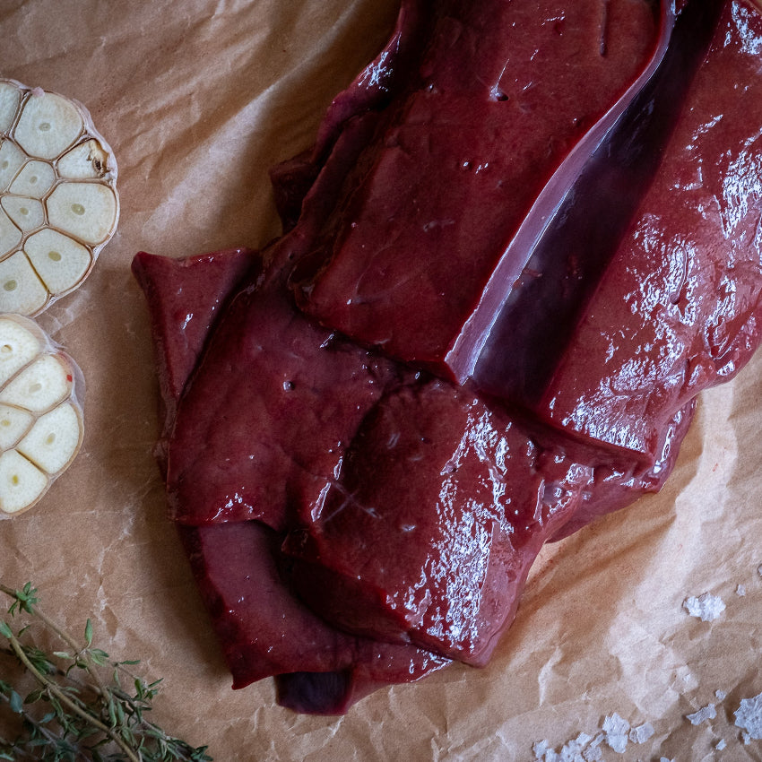 Raw liver slices on a textured surface with garlic and herbs