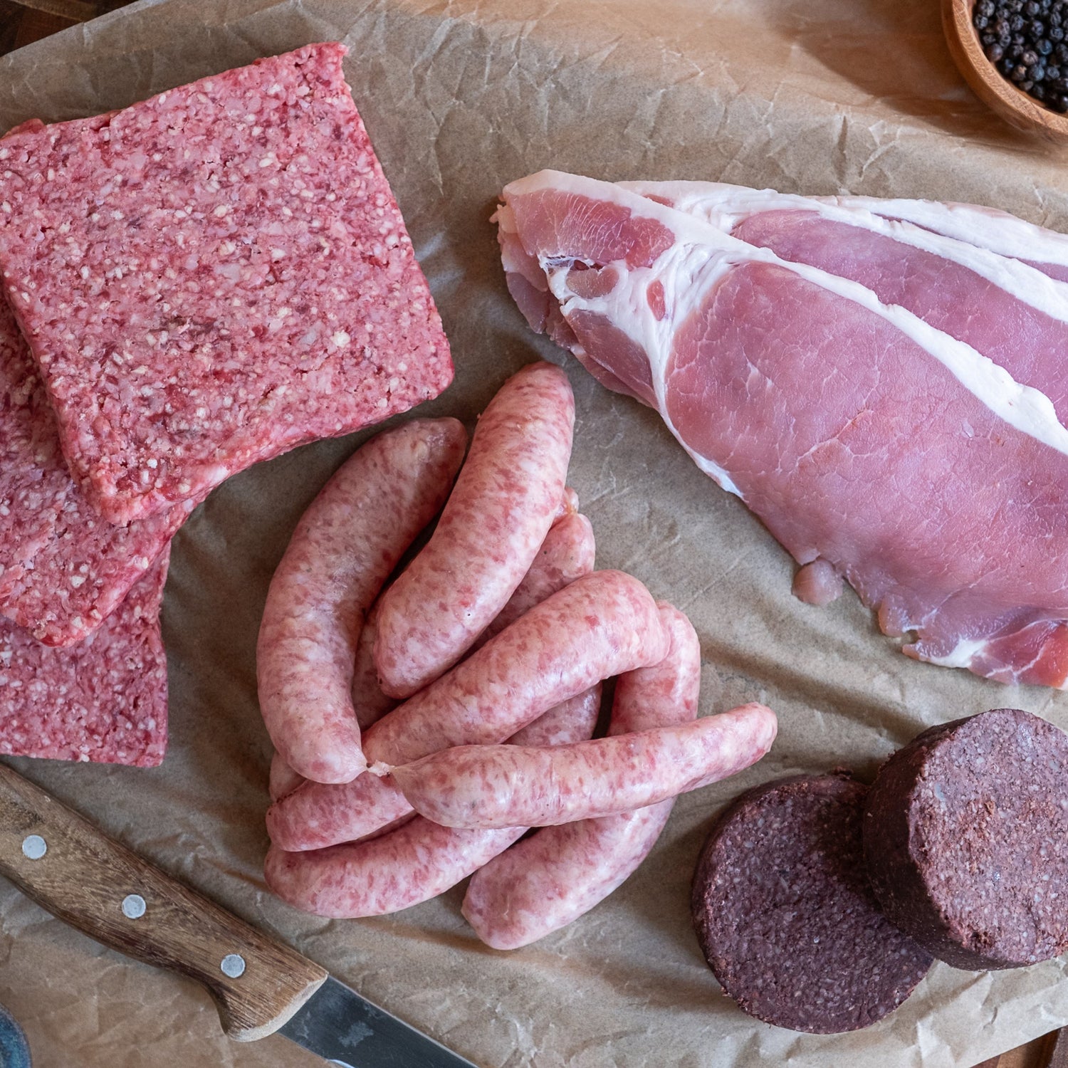 Raw meat products including sausages, ground meat, and cured meat on a wooden surface.