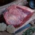 Raw plate of beef on brown paper with garlic, rosemary, and a knife.
