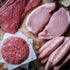 Assorted raw meats including beef, pork, and sausages on a rustic background with tomatoes and garlic.