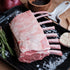 Raw rack of lamb on a black tray with herbs and garlic on a rustic background