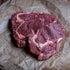 Three raw 50 day aged rib eye steaks with visible marbling, resting on crumpled brown butcher paper over a dark wooden surface.