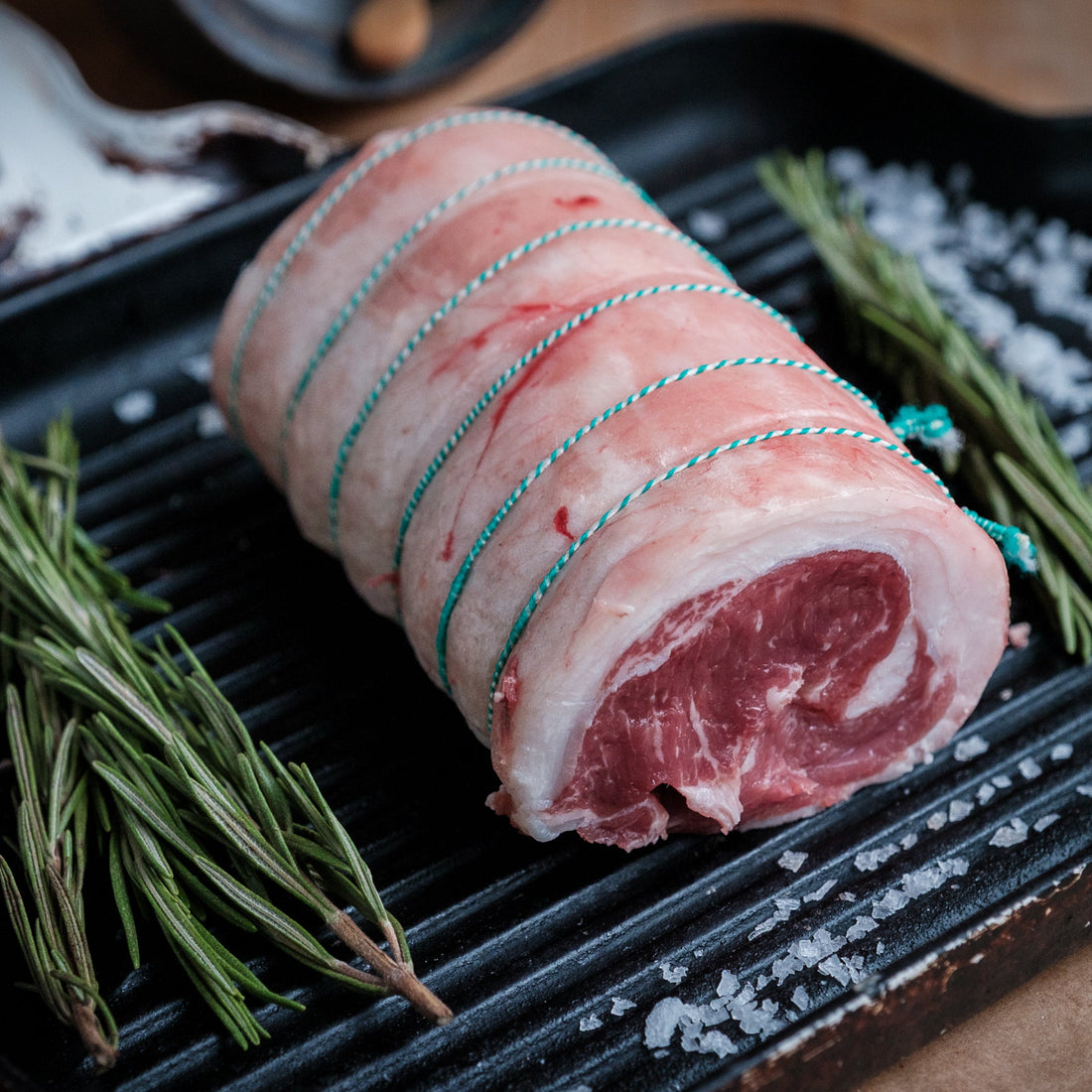 Raw rolled lamb loin l with string on a grill pan with rosemary and salt