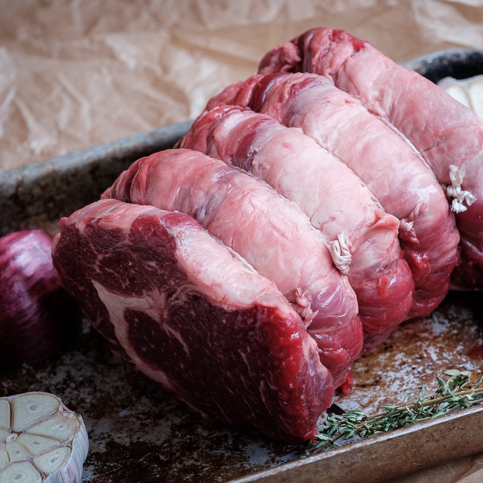 Raw rolled rib eye on a baking tray with onions and garlic