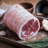 Rolled lamb saddle on a baking tray with garlic and rosemary
