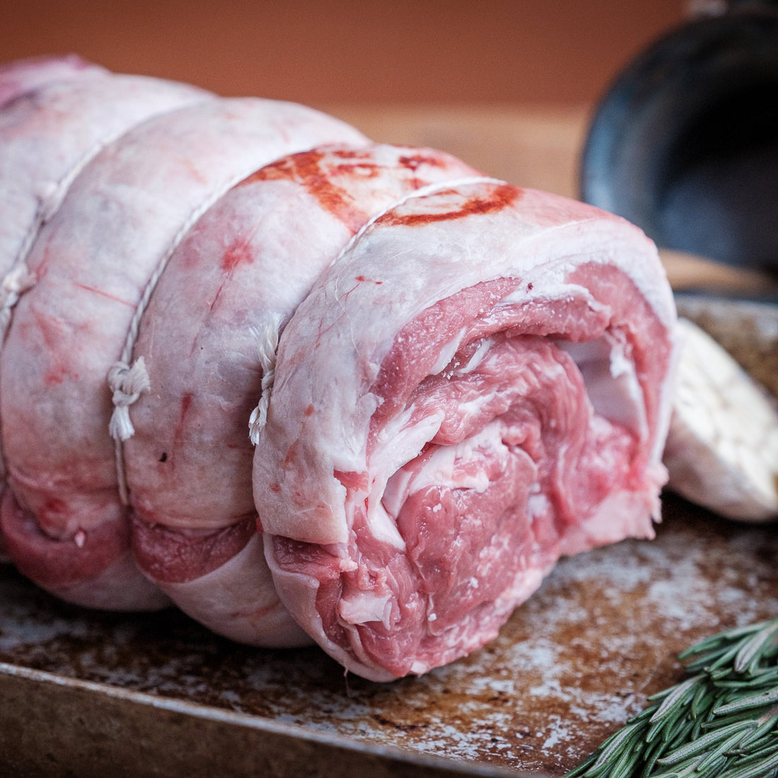Raw rolled lamb shoulder on a rustic surface with herbs and onions