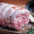Raw rolled lamb shoulder on a rustic surface with herbs and onions