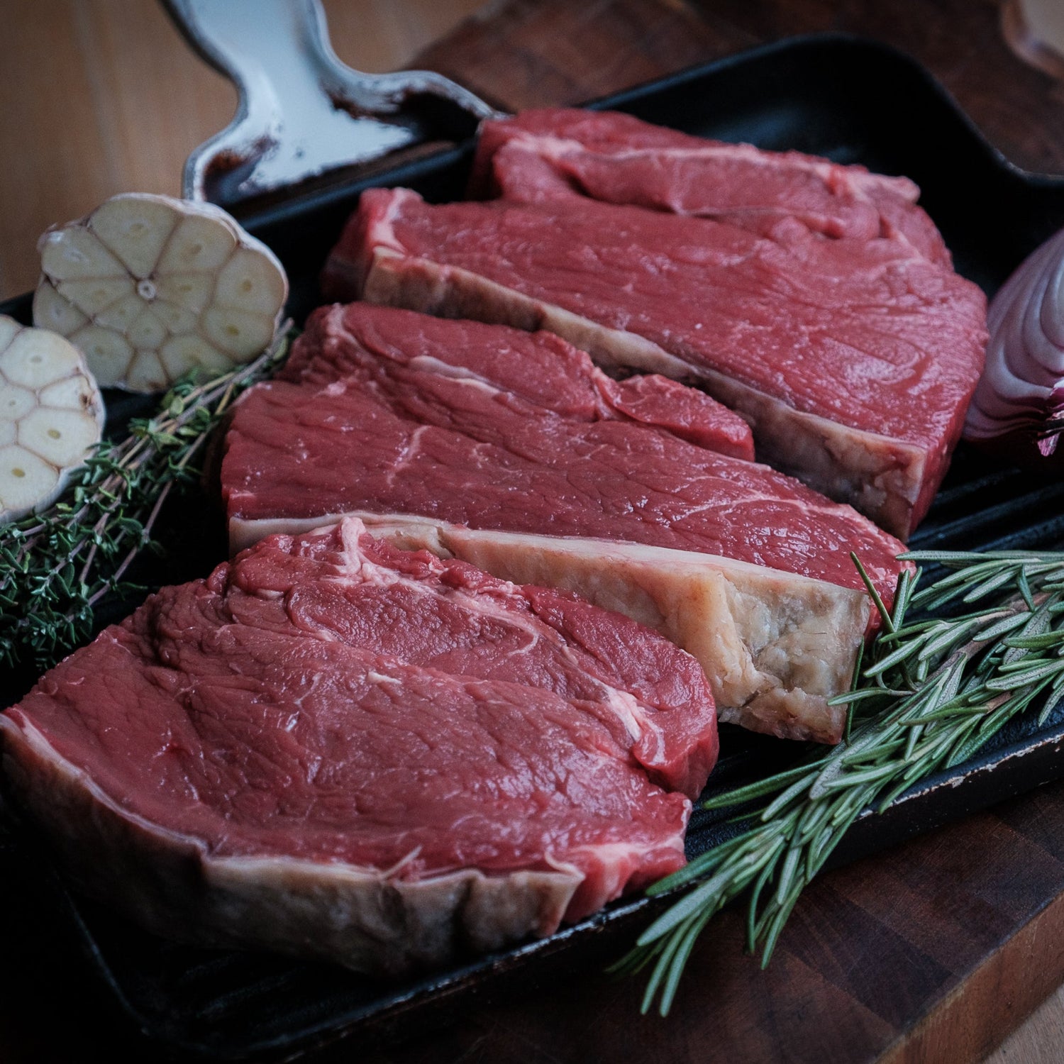 Rump Steak on a skillet with herbs, garlic &amp; onion