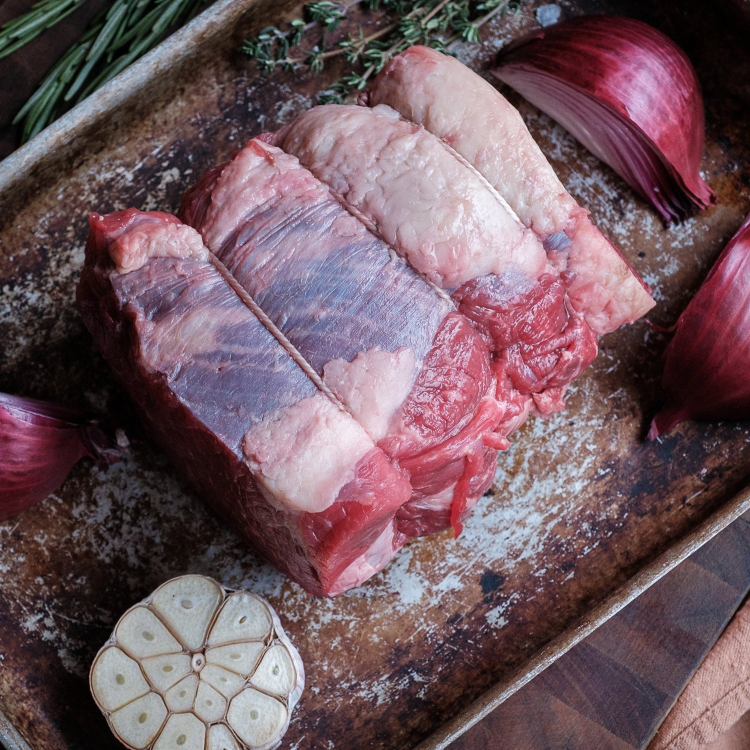 Raw beef silverside on a baking tray with onions and garlic