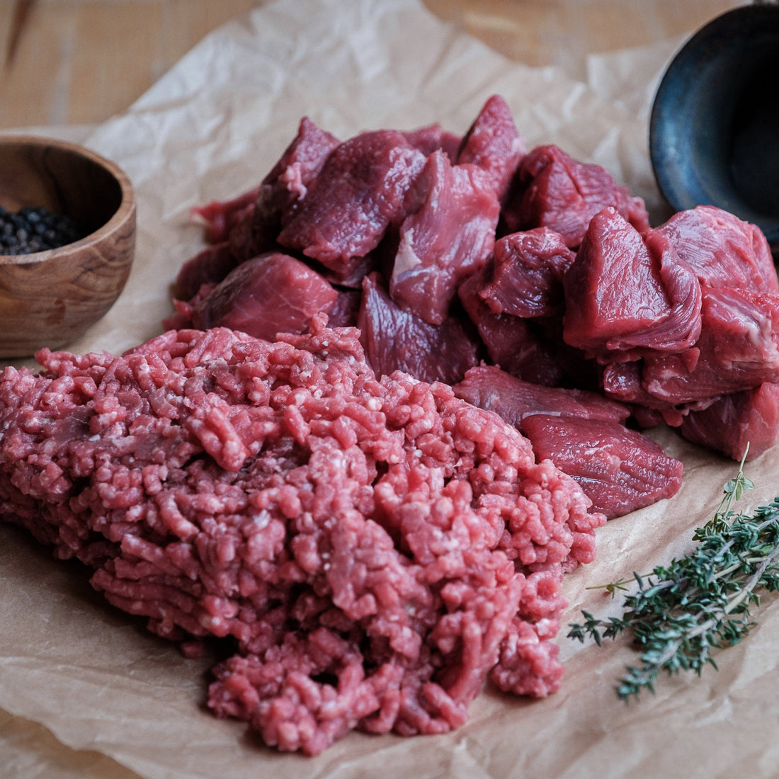Raw ground beef and chopped meat on brown paper with a wooden bowl and black container.