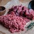 Raw ground beef and chopped meat on brown paper with a wooden bowl and black container.