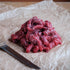 Raw beef stir fry strips and a knife on crumpled paper with a wooden surface.