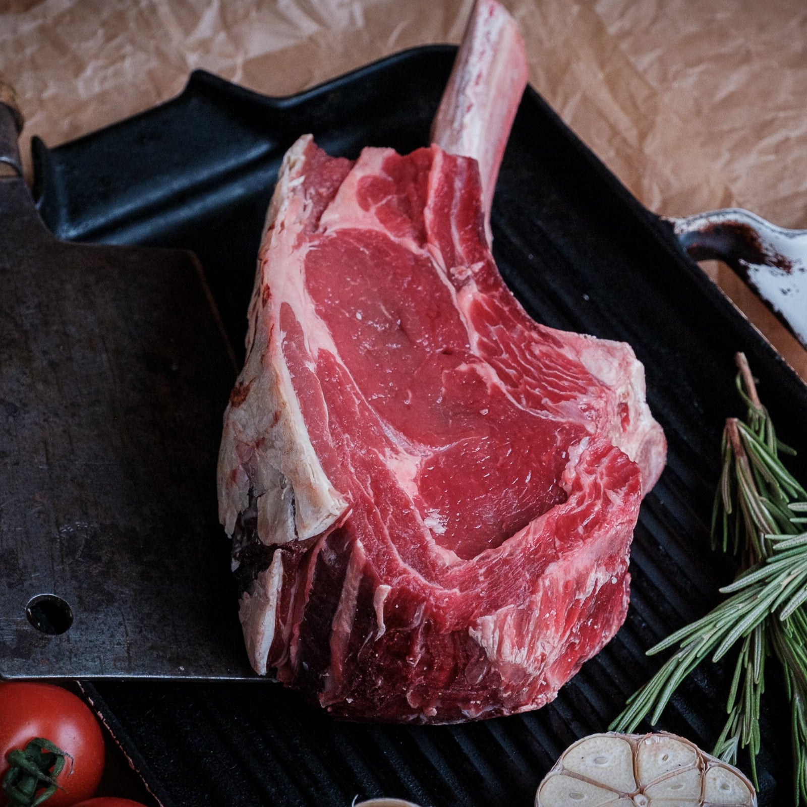 Raw Tomahawk steak on a grill with rosemary and garlic cloves.