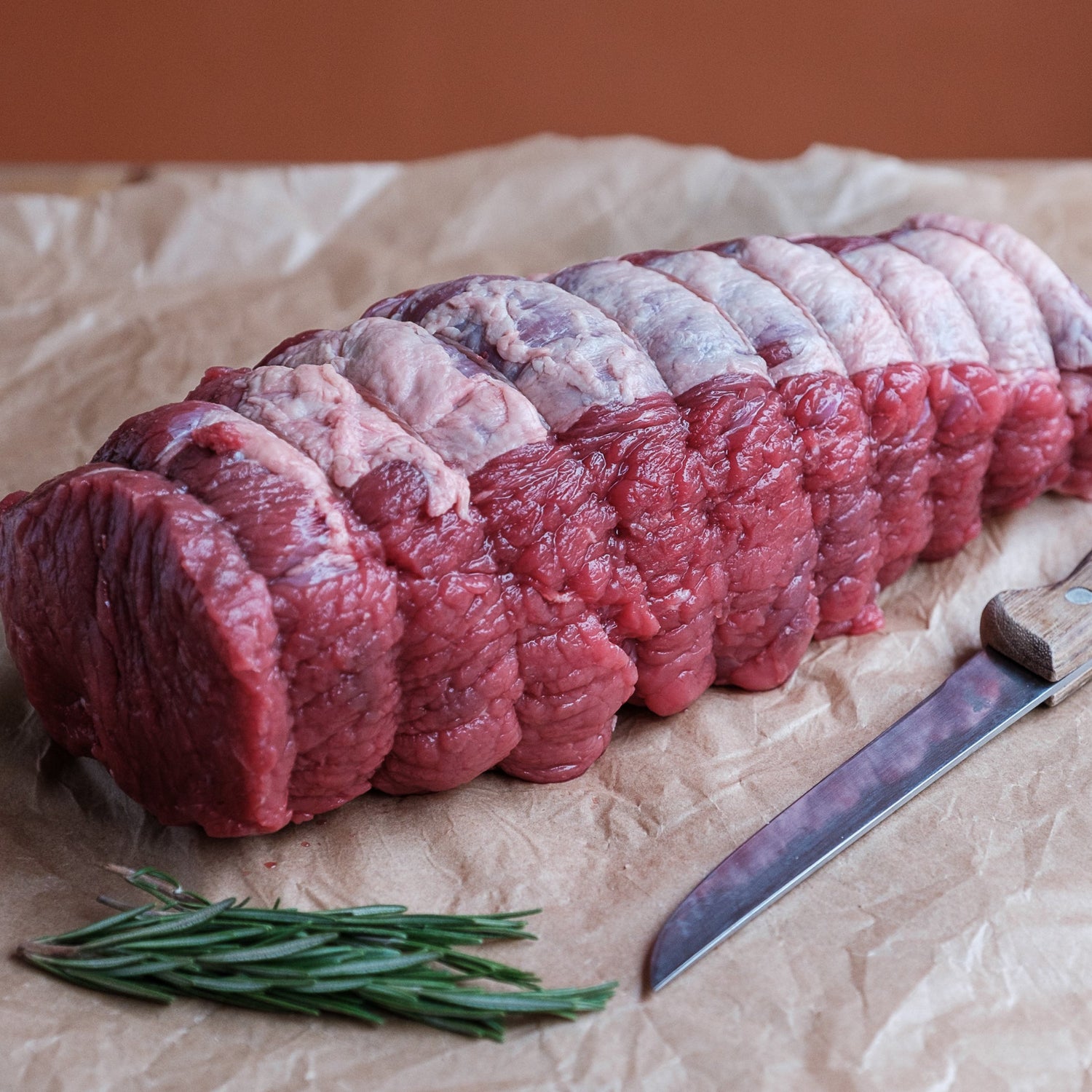 Raw beef topside dry aged for 50 days on crumpled paper with a knife and rosemary.